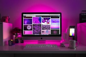 silver-imac-displaying-collage-photos-1779487 Modern desk setup with neon lighting and a desktop computer displaying colorful images.